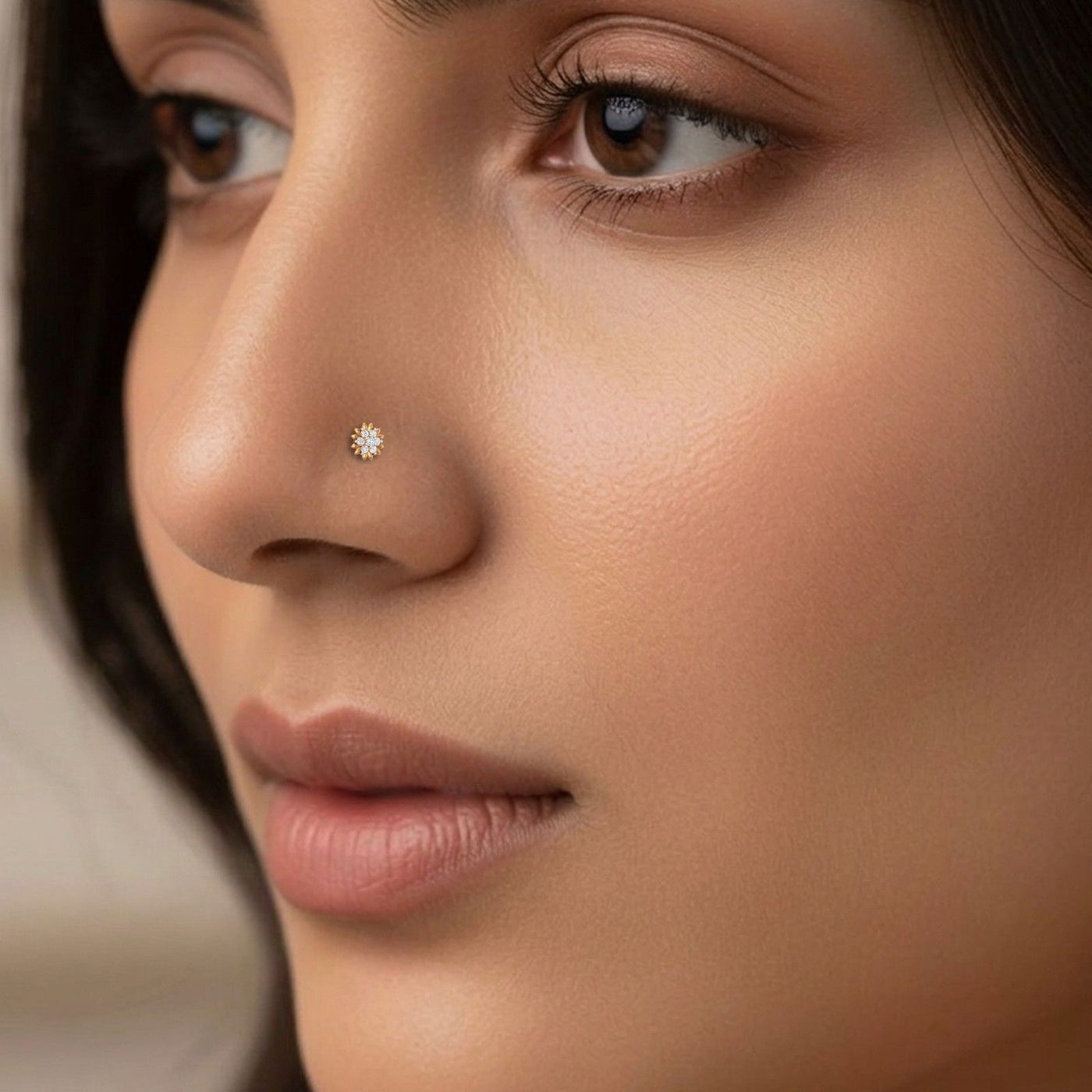 Close-up of a woman's face wearing a small gold nose pin with a floral or starburst design.