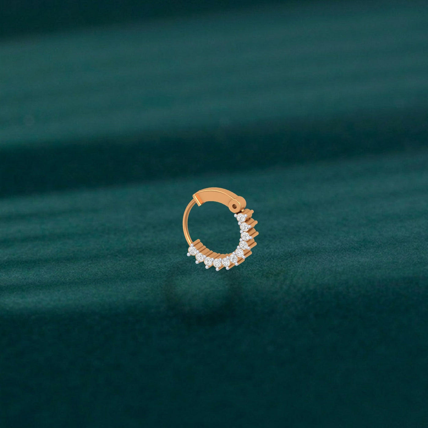 Yellow gold and diamond nose ring on a green fabric background