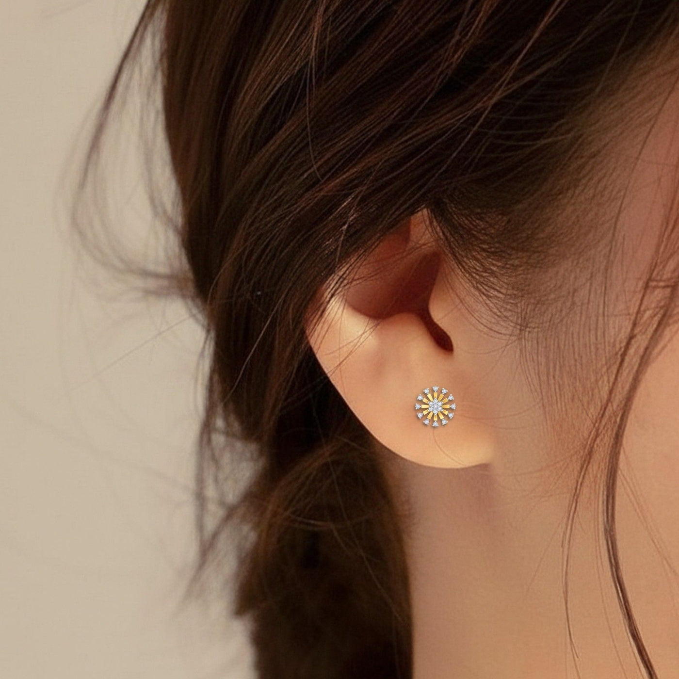 Close-up of an ear wearing a decorative gold and diamond stud earring with a neutral background.