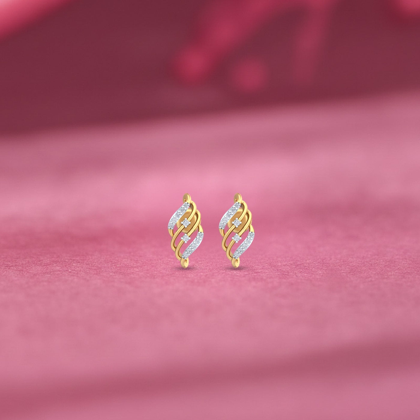 Gold and diamond stud earrings on a pink fabric background
