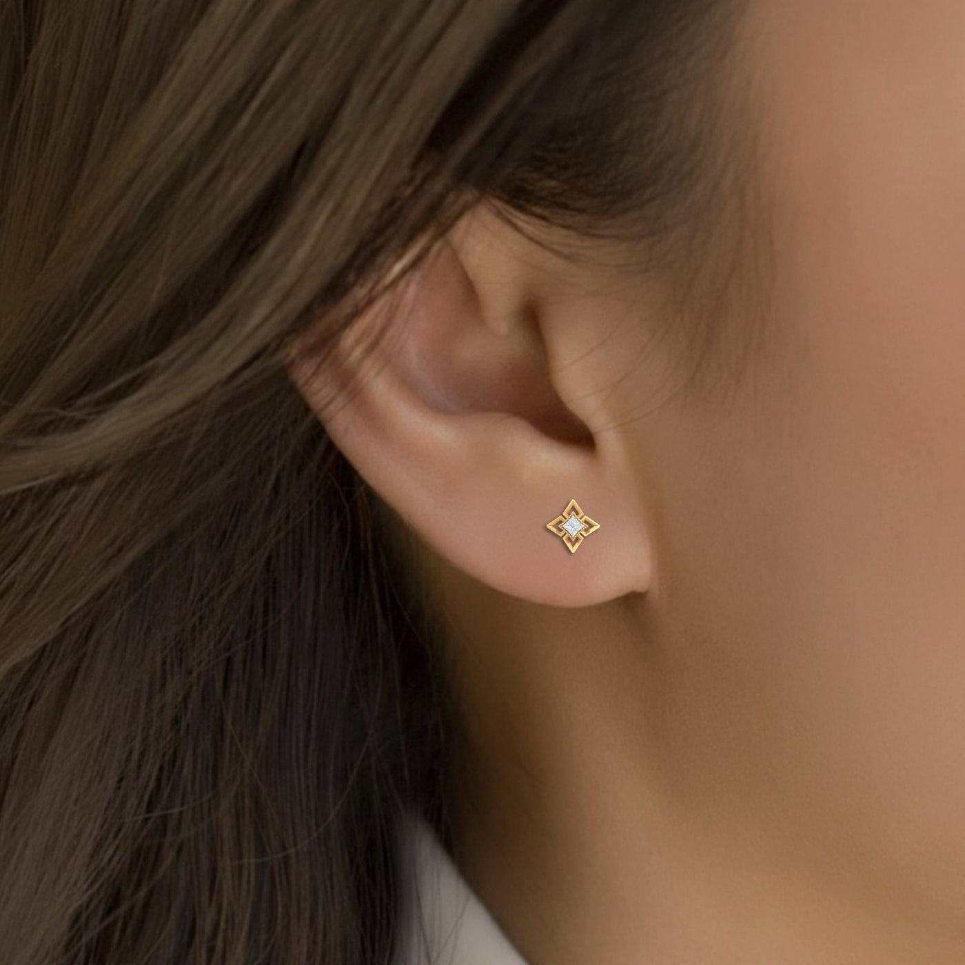 Close-up of an ear wearing a gold and diamond stud earring.
