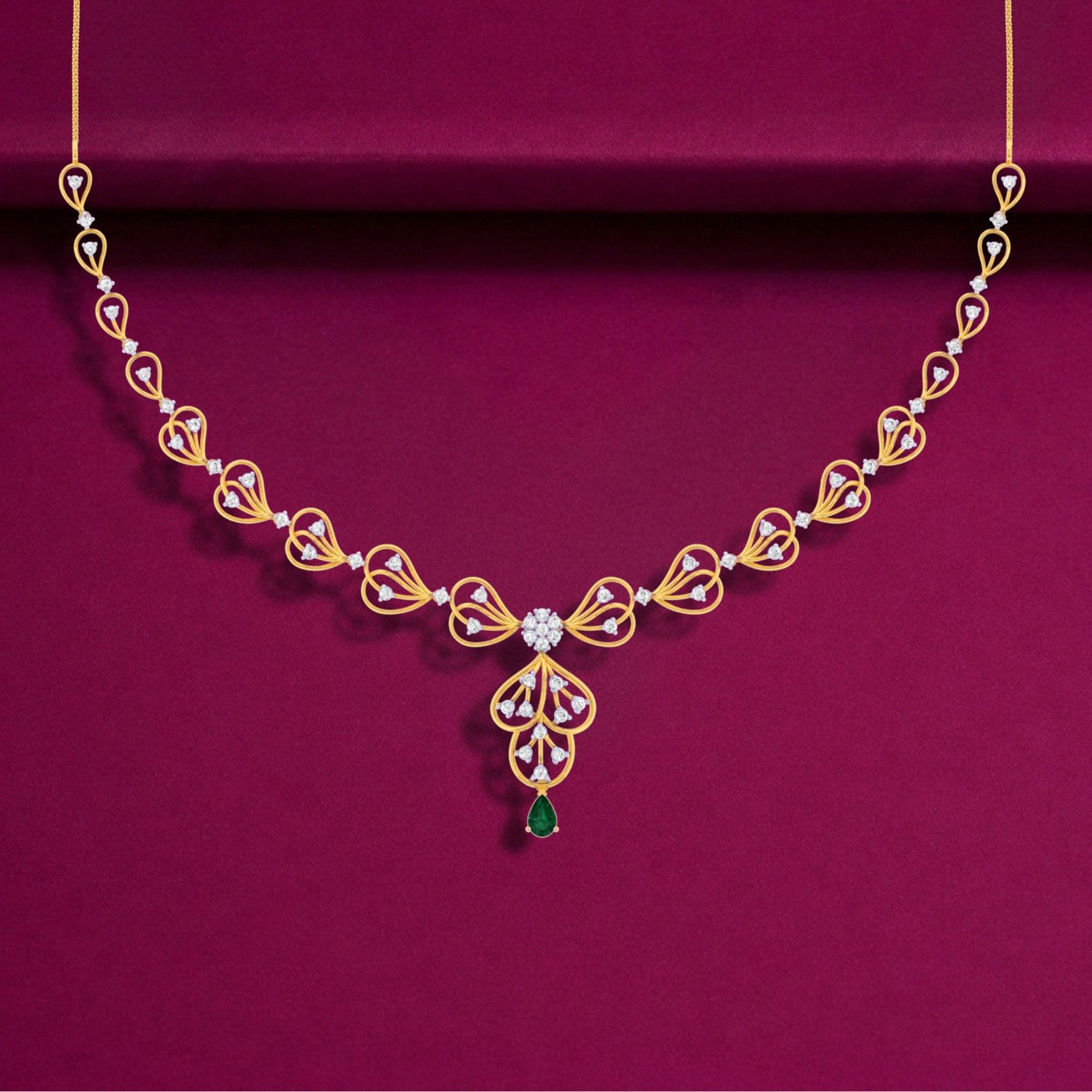 Gold and diamond necklace with green teardrop gemstone, displayed on a deep magenta background.