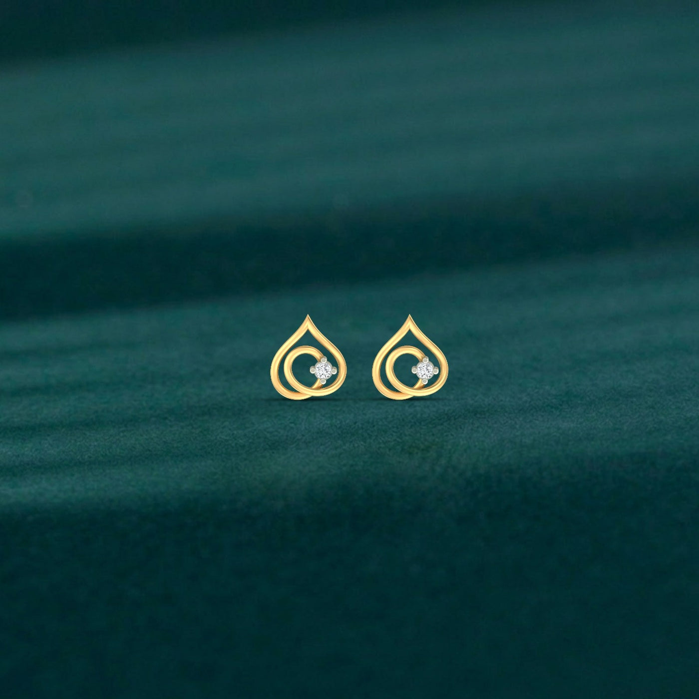 Gold and diamond teardrop-shaped stud earrings on a green fabric background