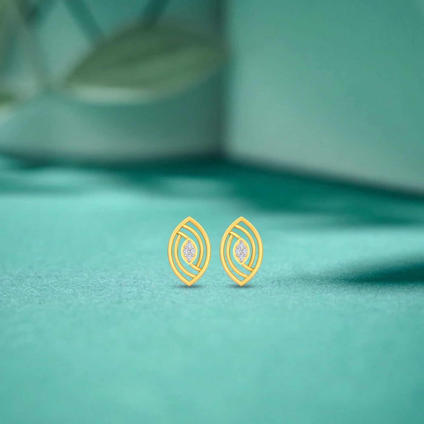 A pair of gold-toned geometric stud earrings diamonds in the center, resting on a textured teal surface.