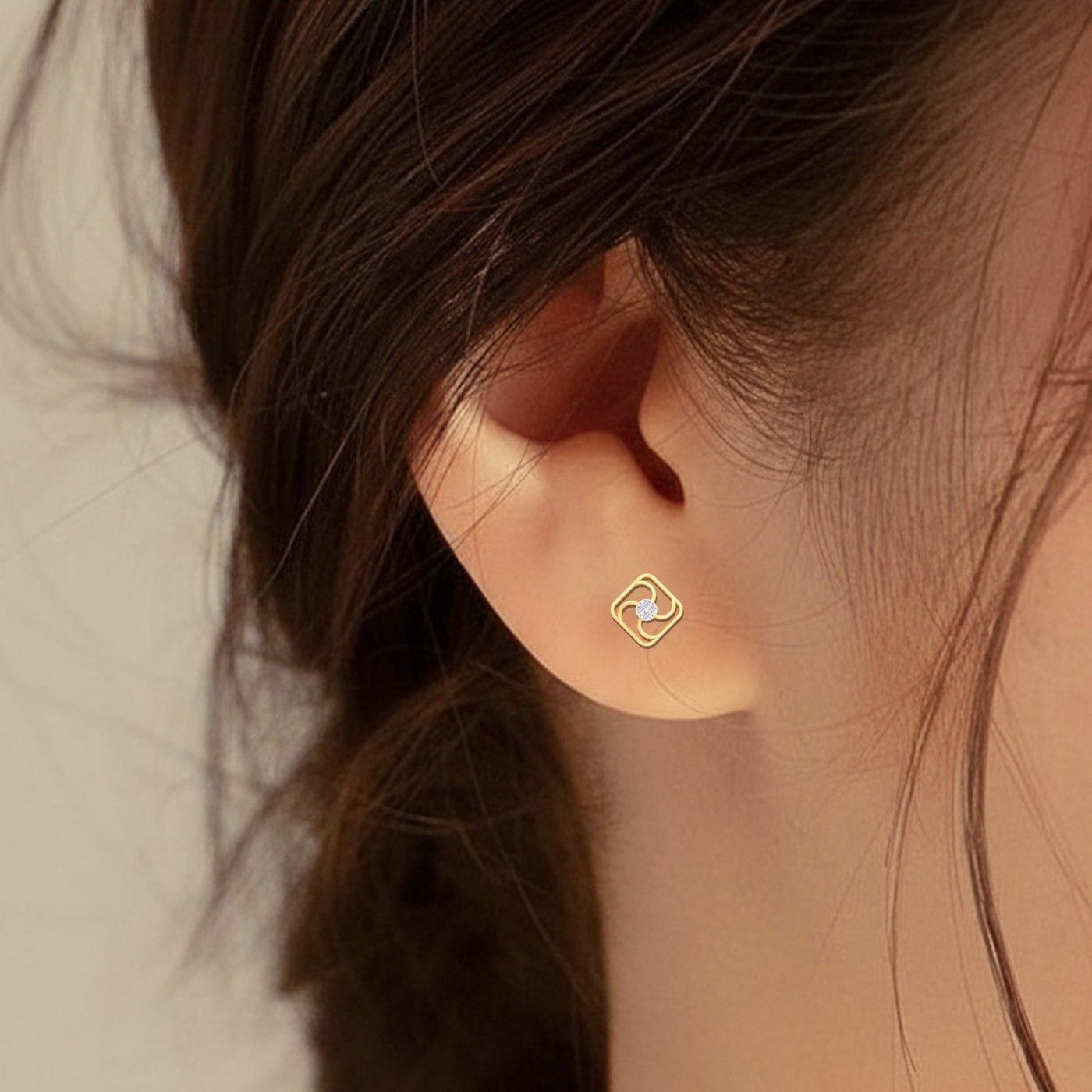 Close-up of an ear wearing a gold and diamond stud earring.