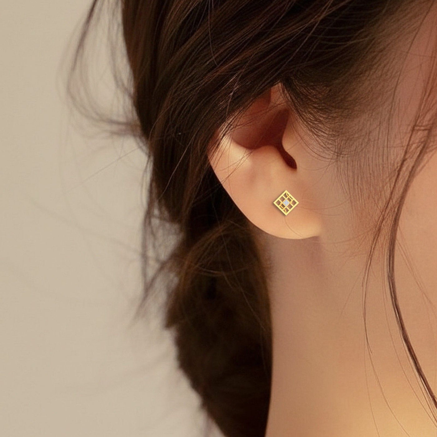 Gold and diamond geometric stud earring worn by a person.