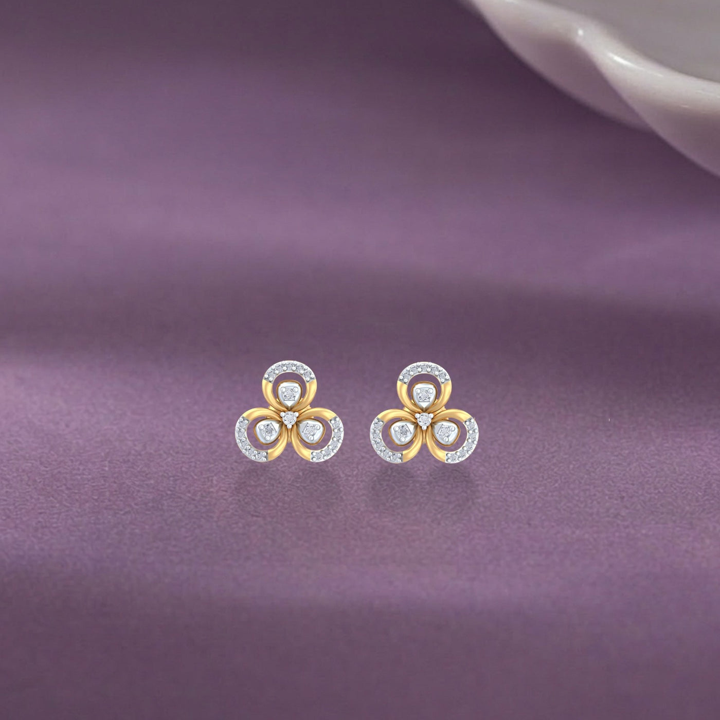 Gold and diamond floral stud earrings on a purple fabric background