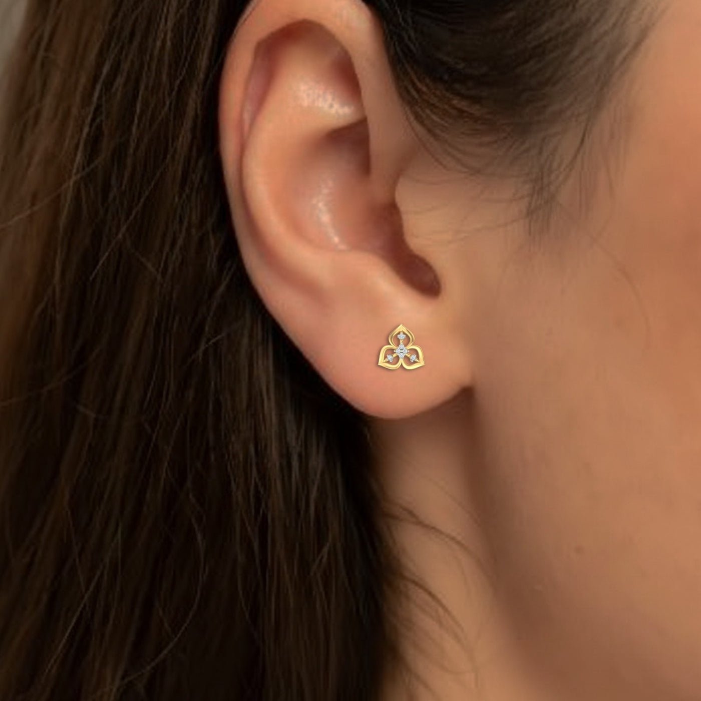 Close-up of an ear wearing a gold and diamond stud earring.
