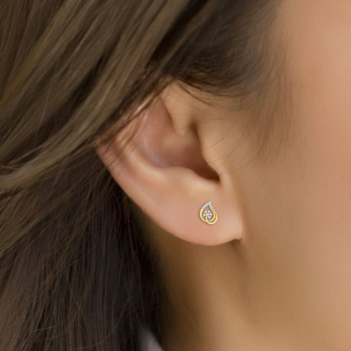 Close-up of an ear wearing a gold and diamond stud earring.