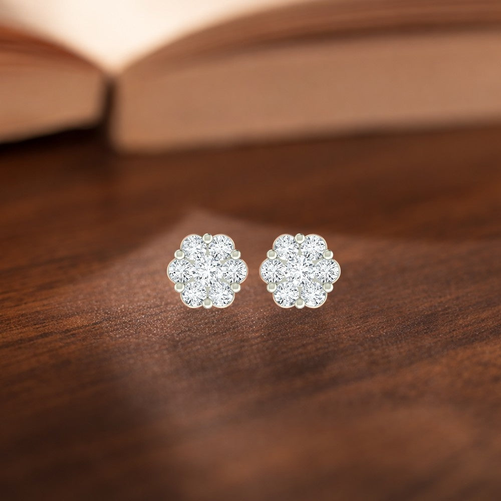 Pair of gold floral earrings on a wooden surface with a blurred book in the background.
