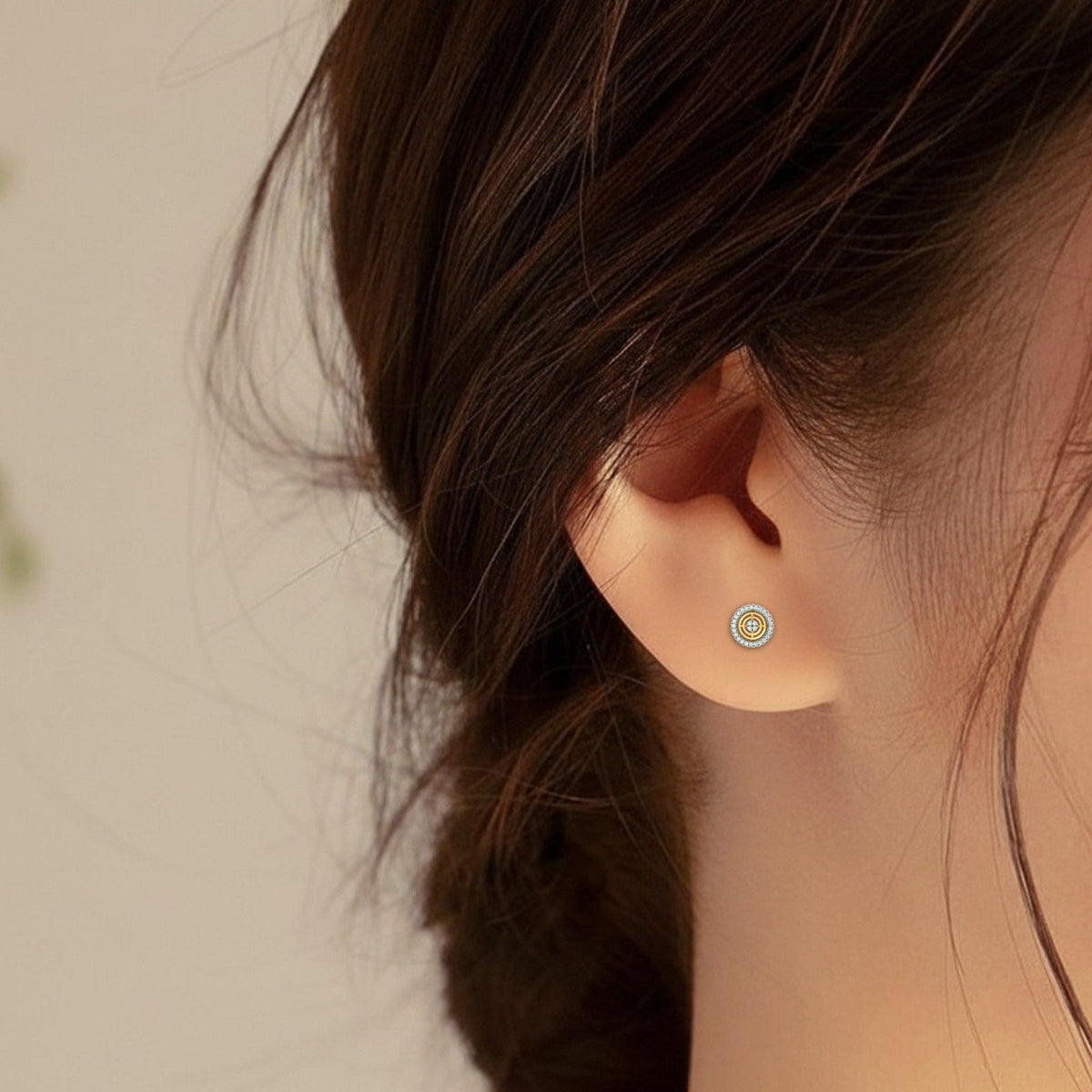 A close-up of a person's ear wearing a Yellow gold and diamond stud earring with round-shaped.