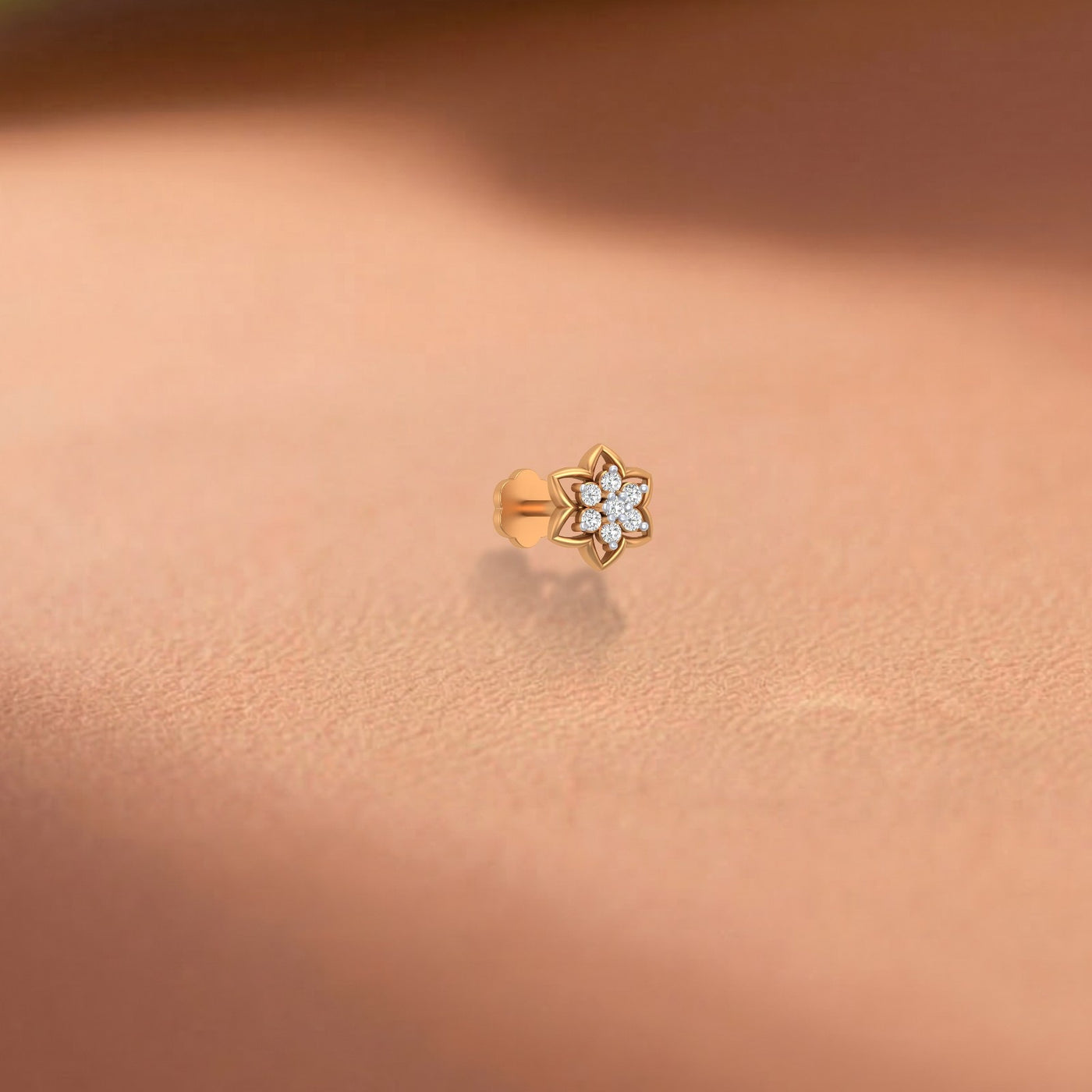 Yellow gold and diamond stud nose pin with clear gemstones on a rose gold background