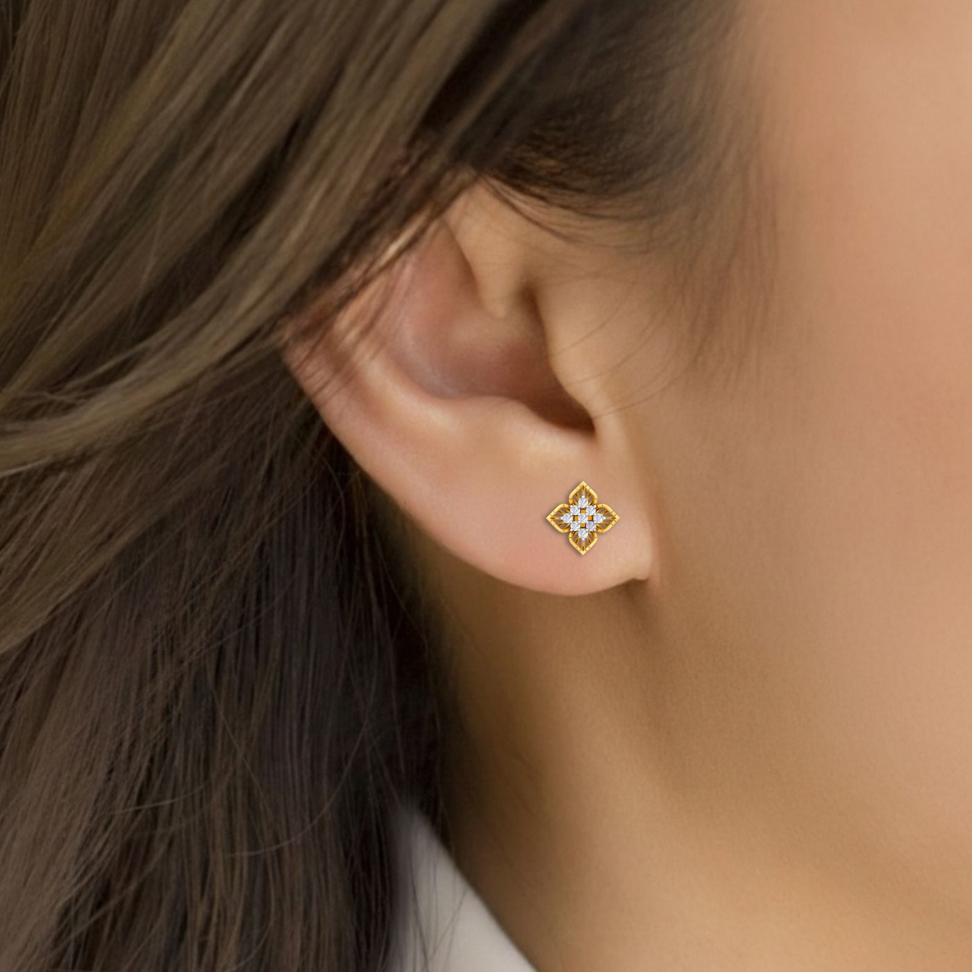 Close-up of an ear wearing a gold and diamond floral-shaped stud earrings