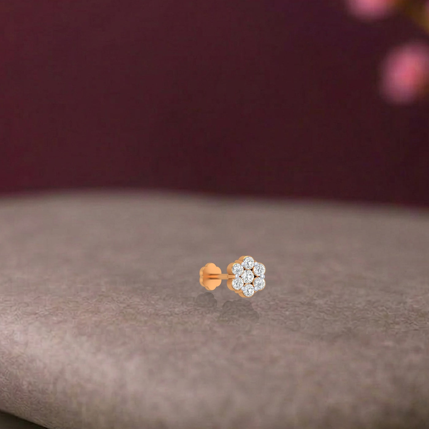 Yellow gold and diamond stud nose pin with clear gemstones on a brown surface