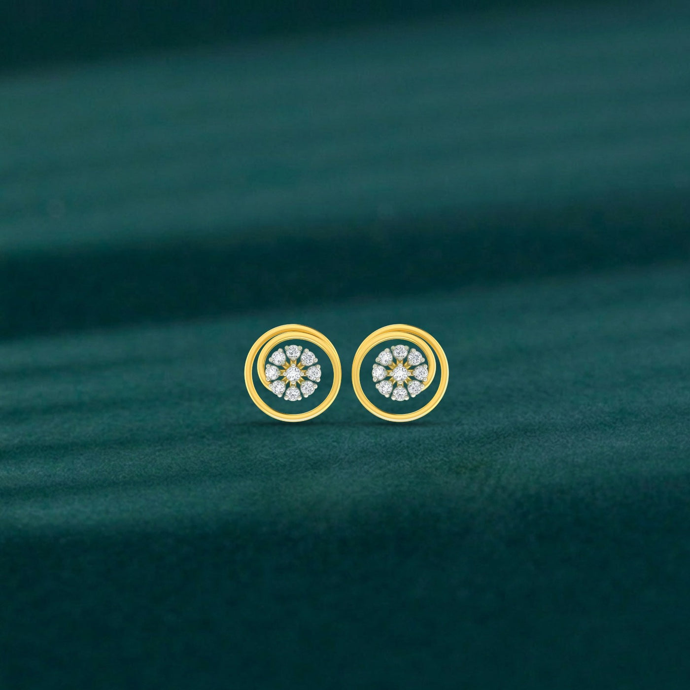 Gold and diamond stud earrings with circular designs on a green fabric background