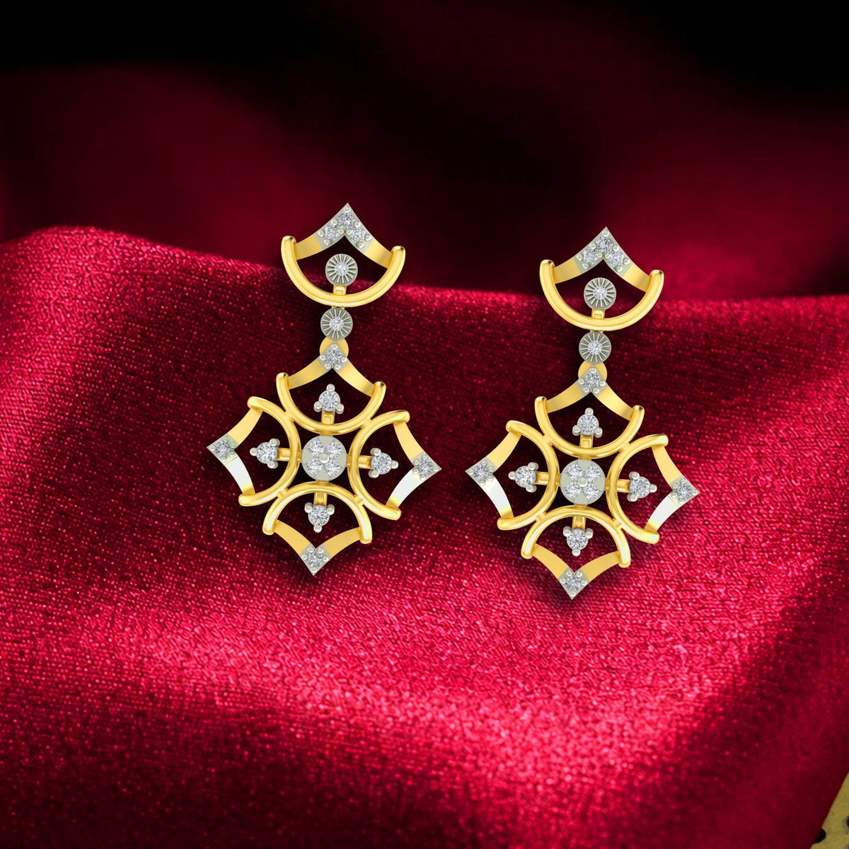 A pair of gold and diamond drop earrings with clear stones, displayed on a rich red satin fabric background.