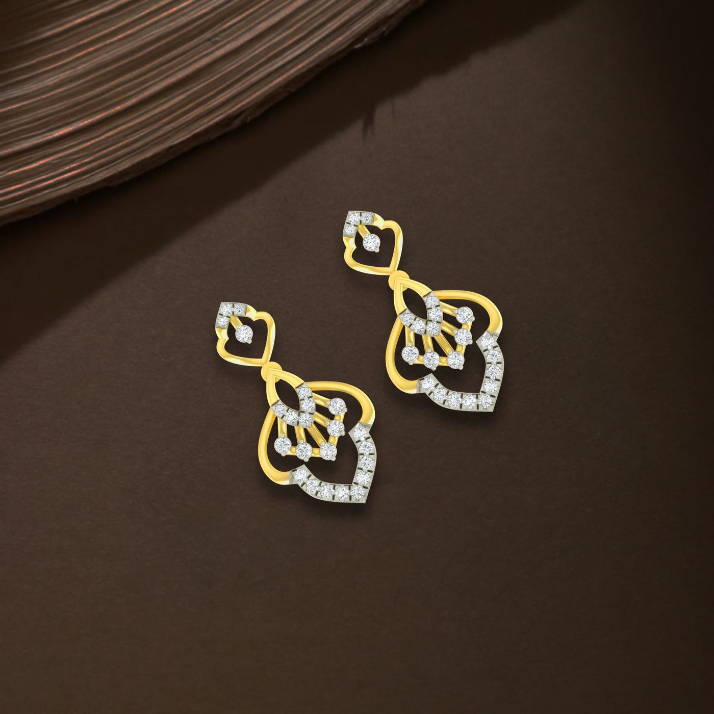 A pair of gold and diamond stone earrings with a floral and geometric design, displayed on a dark brown textured surface.