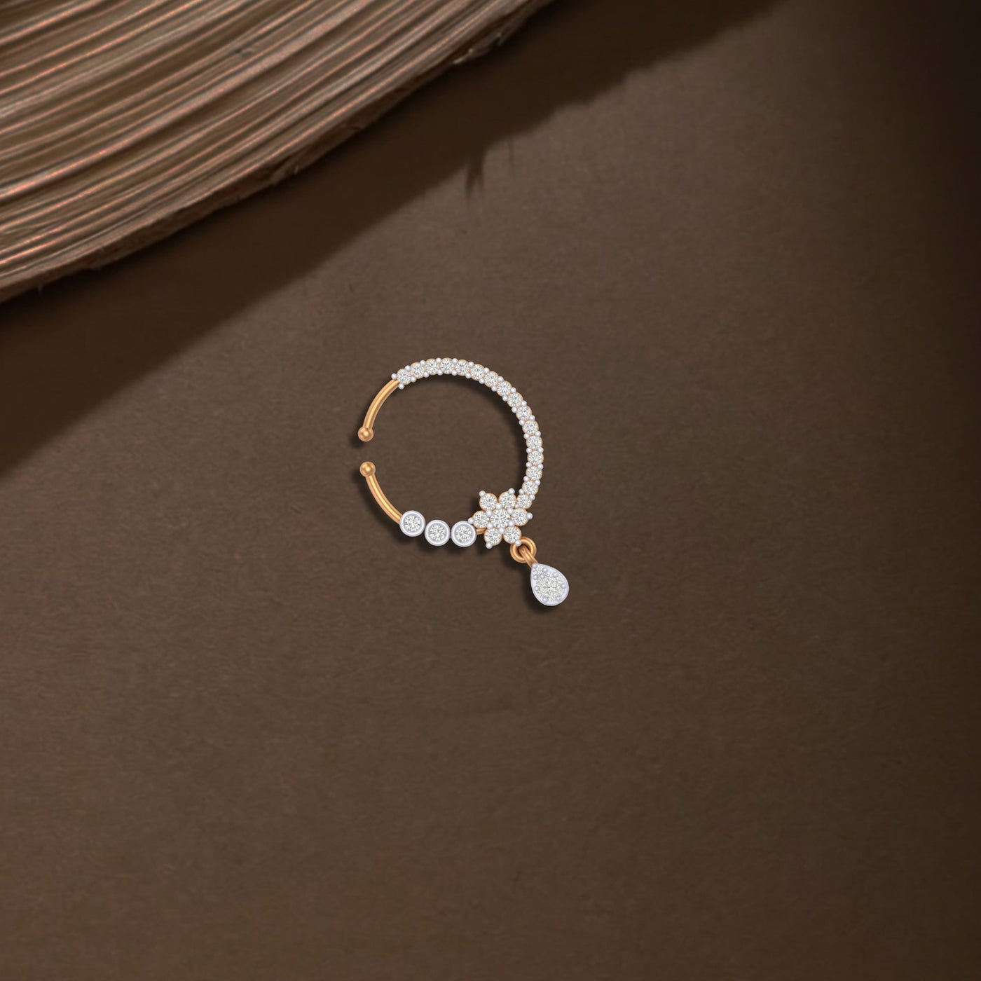 Yellow gold and diamond nose ring with a small charm on a brown surface