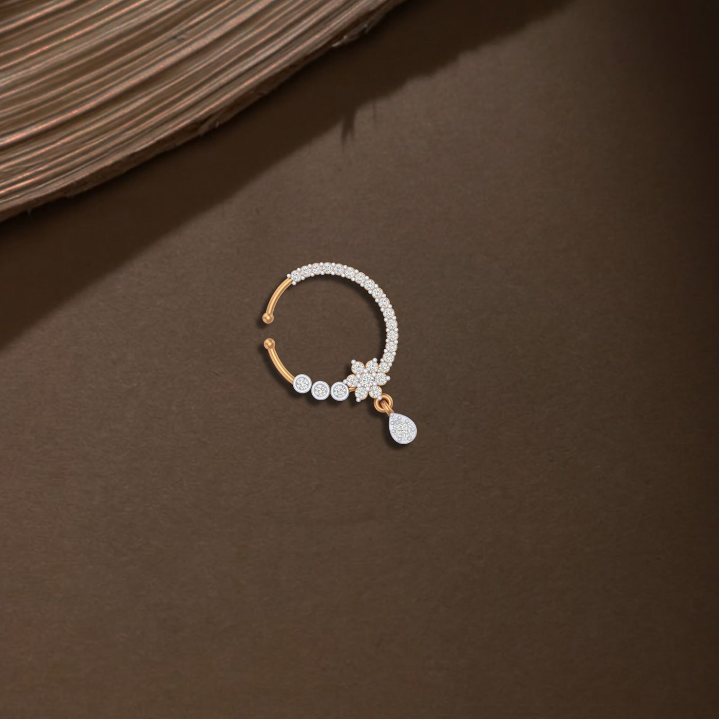 yellow golad and diamond nose ring with a small charm on a brown surface