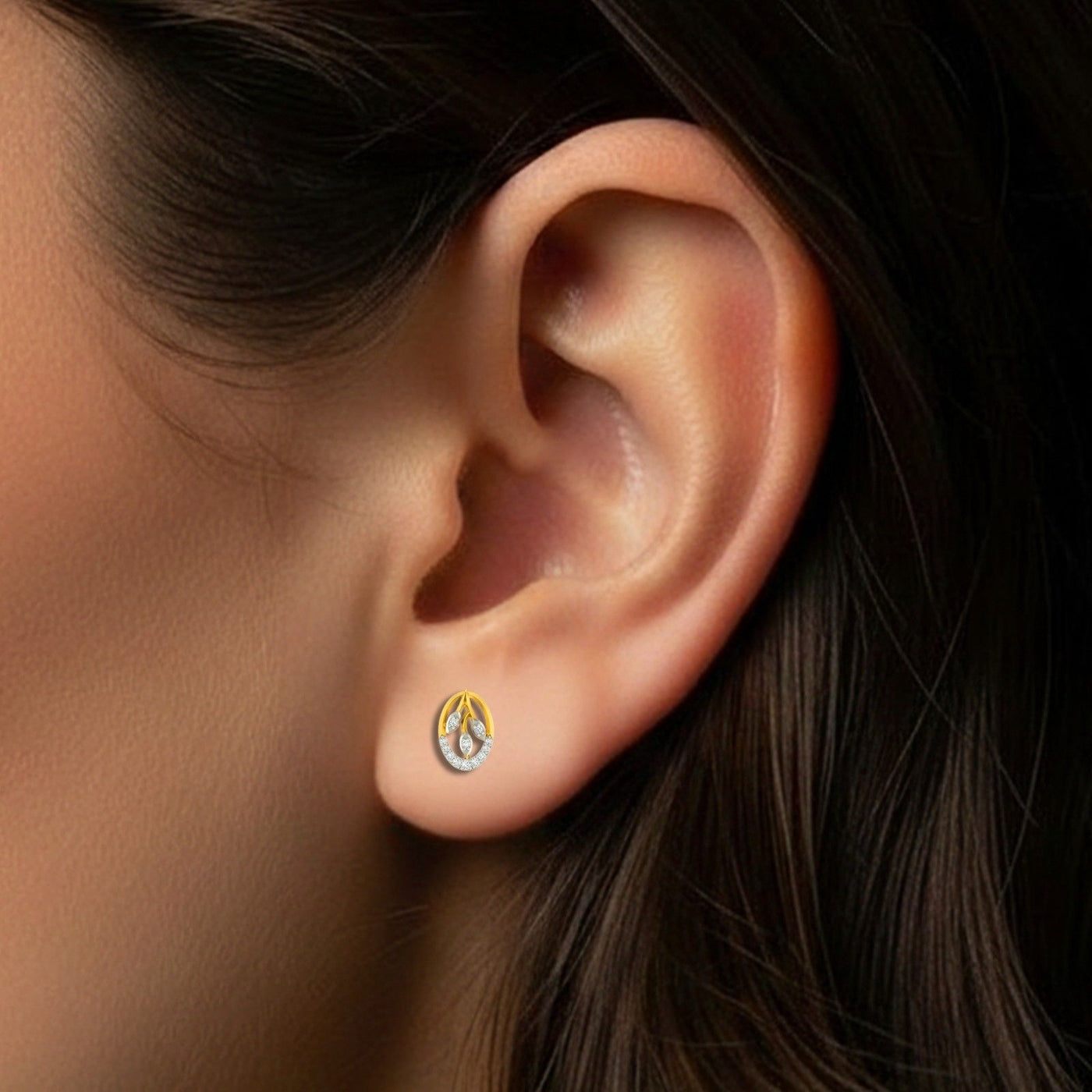 A close-up of a person's ear wearing a small round stud earring with a yellow-gold outer ring.