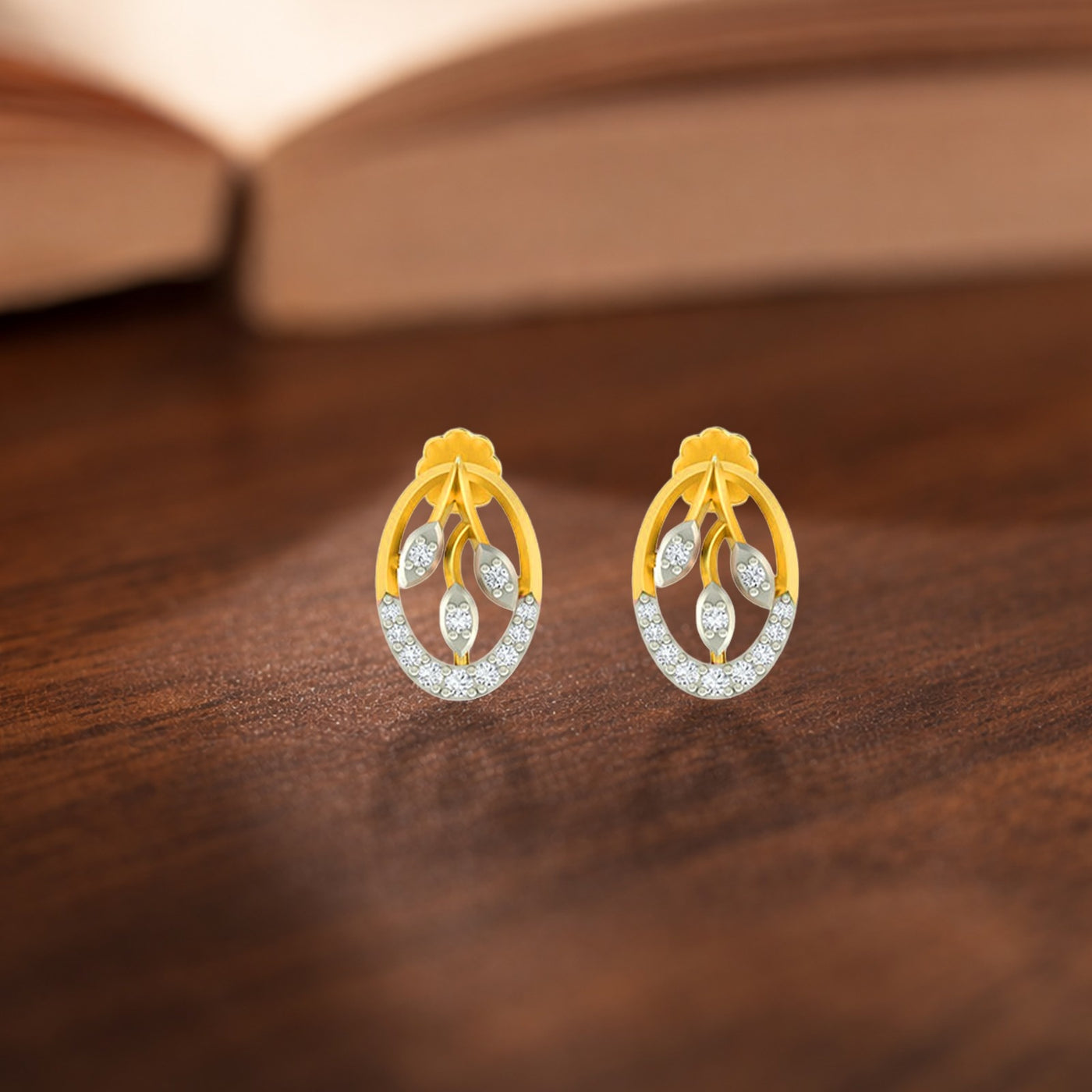 A pair of gold and diamond stud earrings with diamond, displayed on a dark wooden surface with a blurred book in the background.