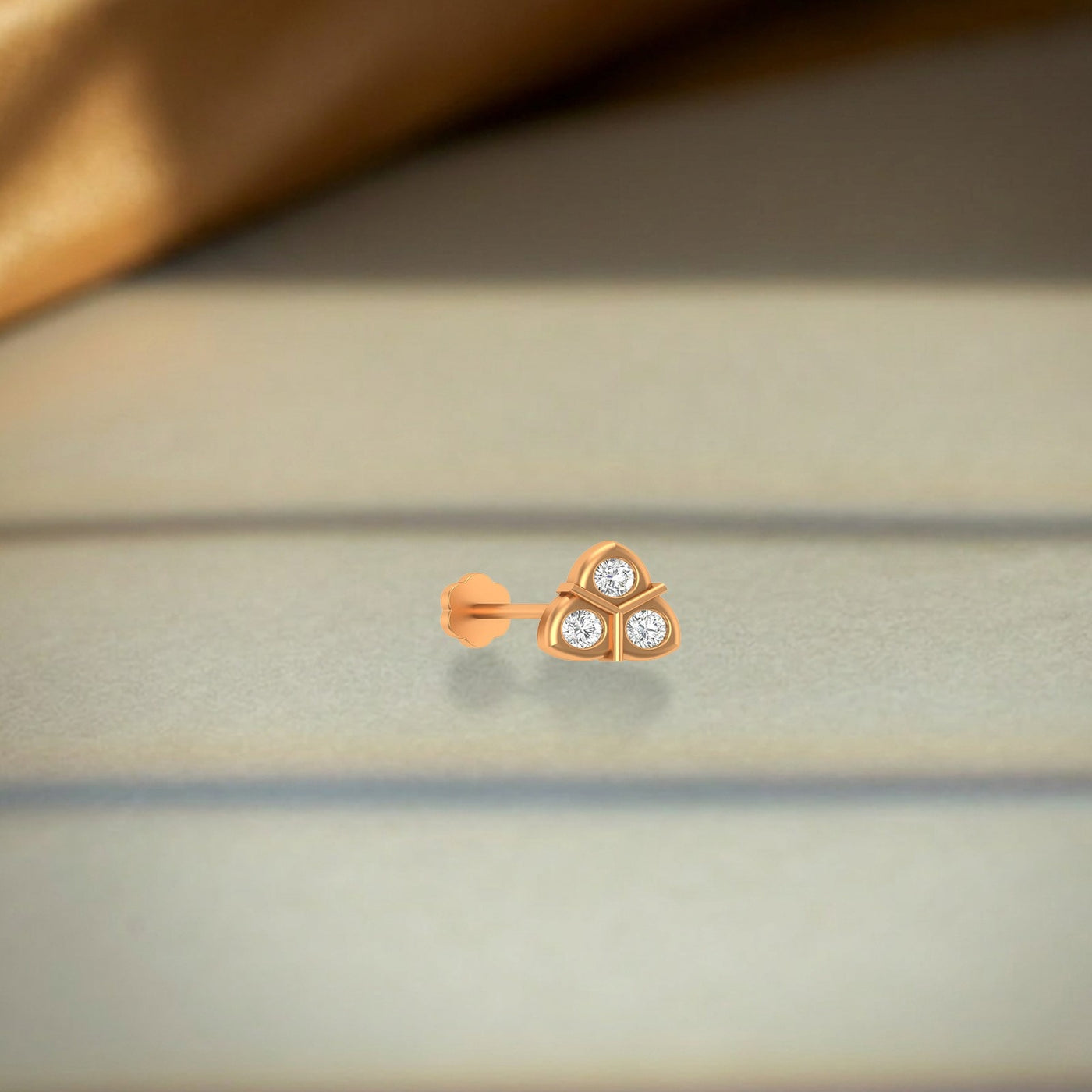 Yellow gold and diamond stud nose pin with three diamonds on a neutral background