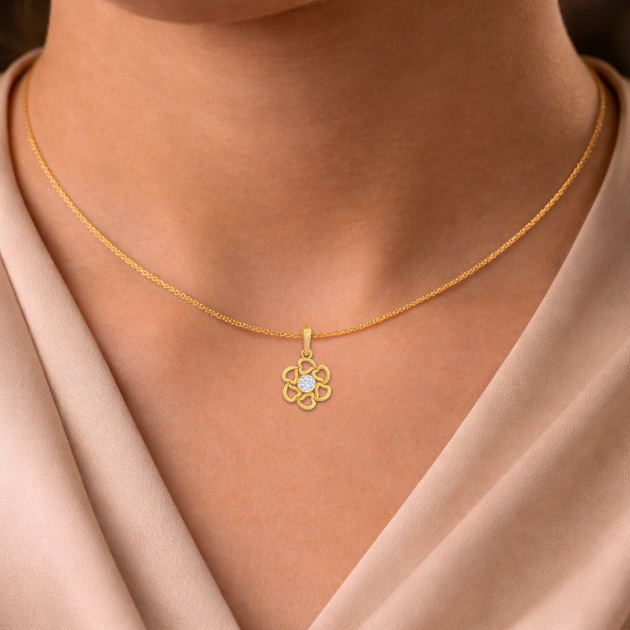 Gold necklace with a floral pendant on a person wearing a beige top.