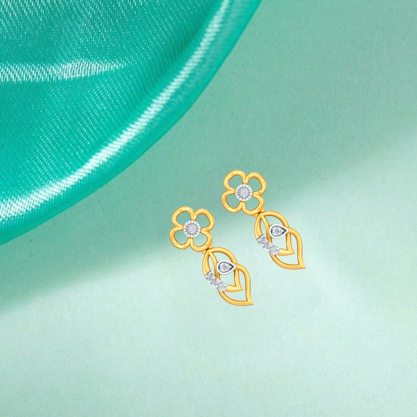 Gold and diamond earrings on a light green fabric background.
