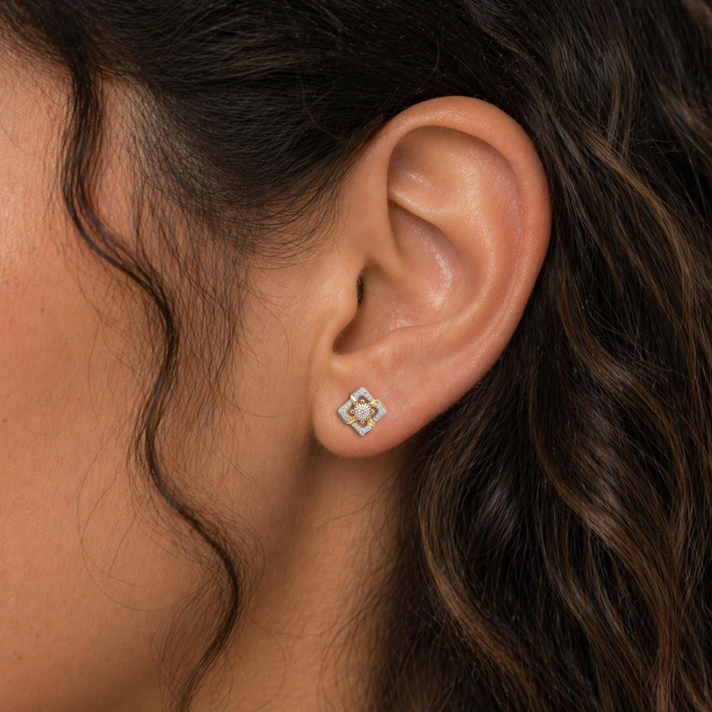 Close-up shot of an ear wearing a gold earrings with diamond-like stones earring.
