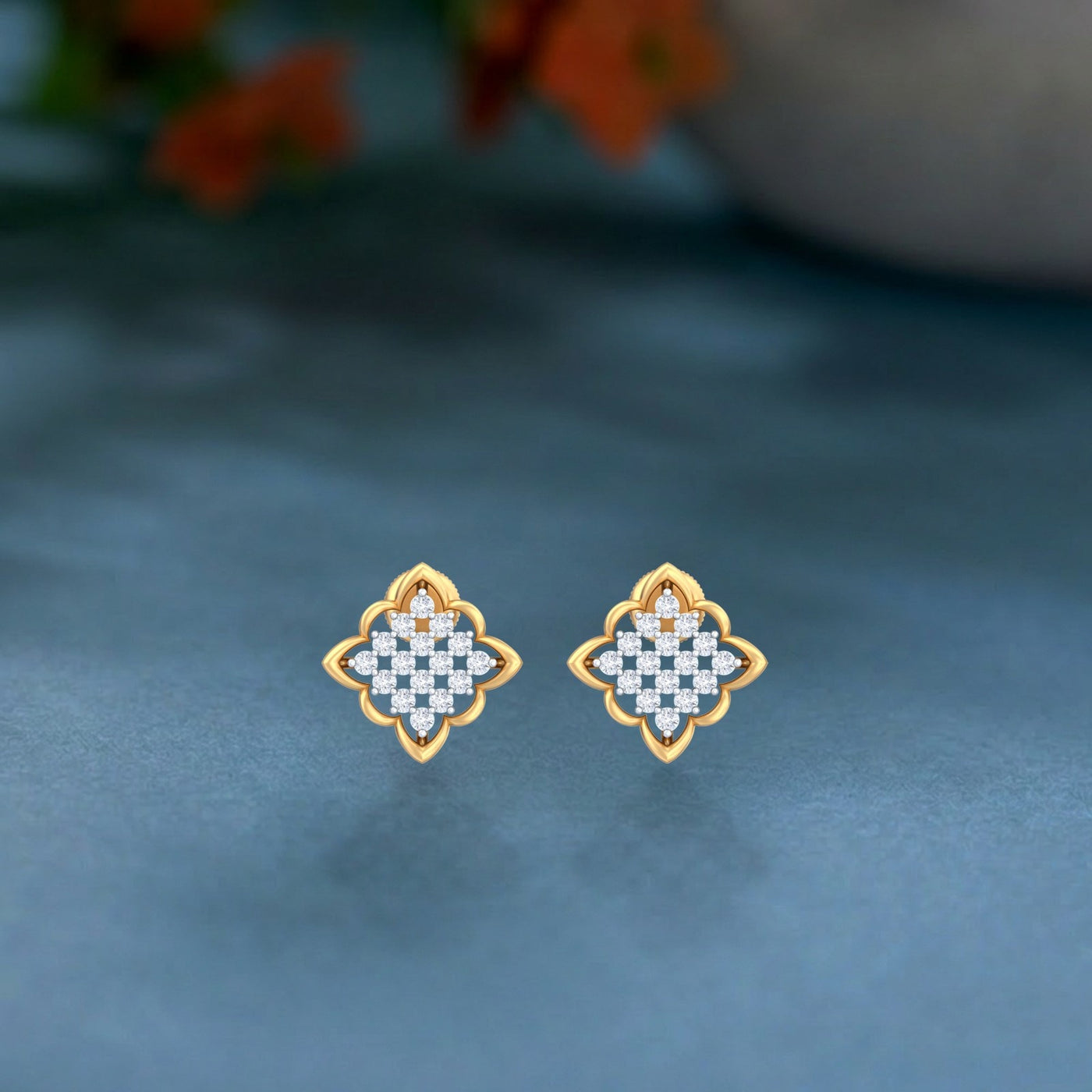 Pair of gold and diamond stud earring with floral-shaped on a teal background