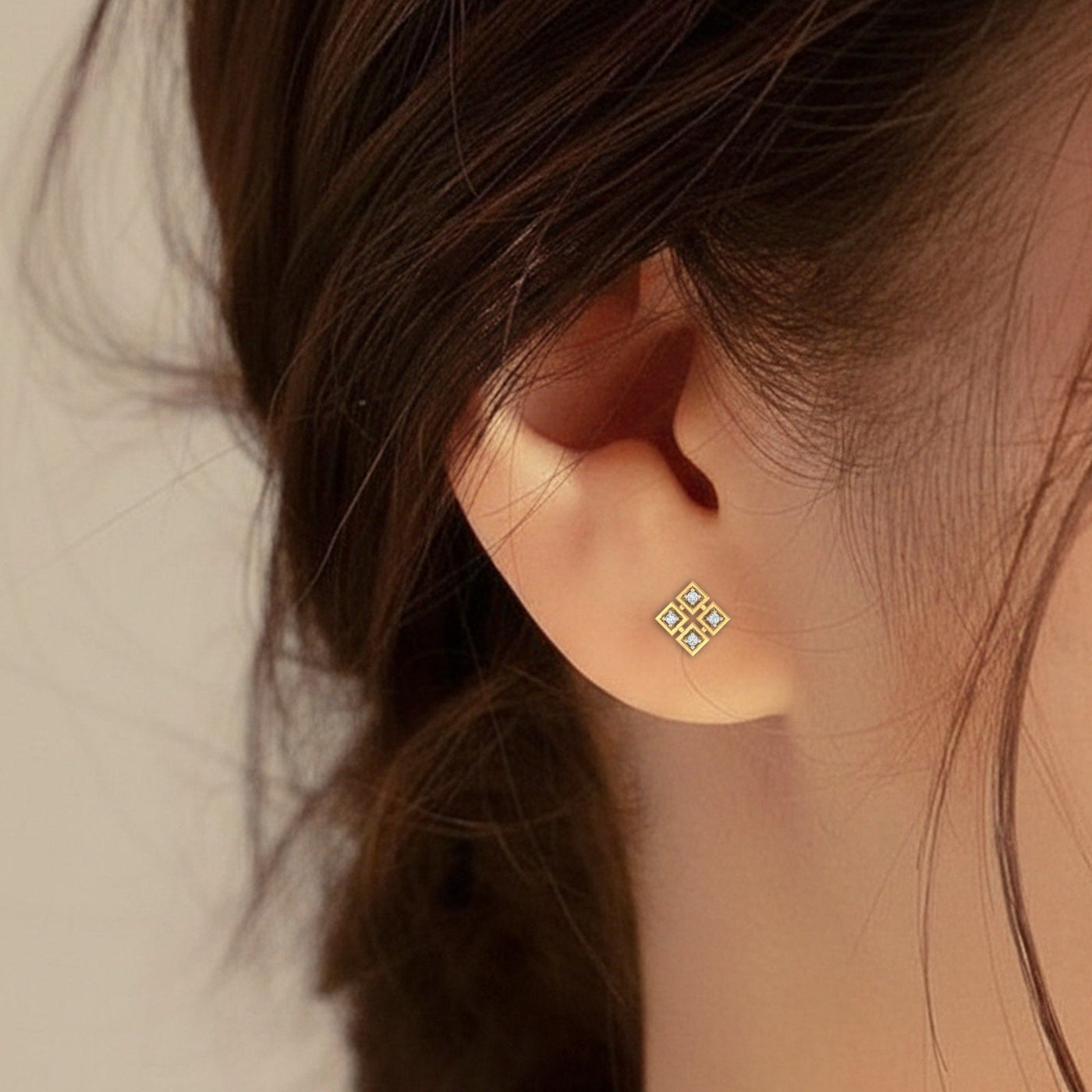 Close-up of an ear wearing a gold earring with a geometric design.