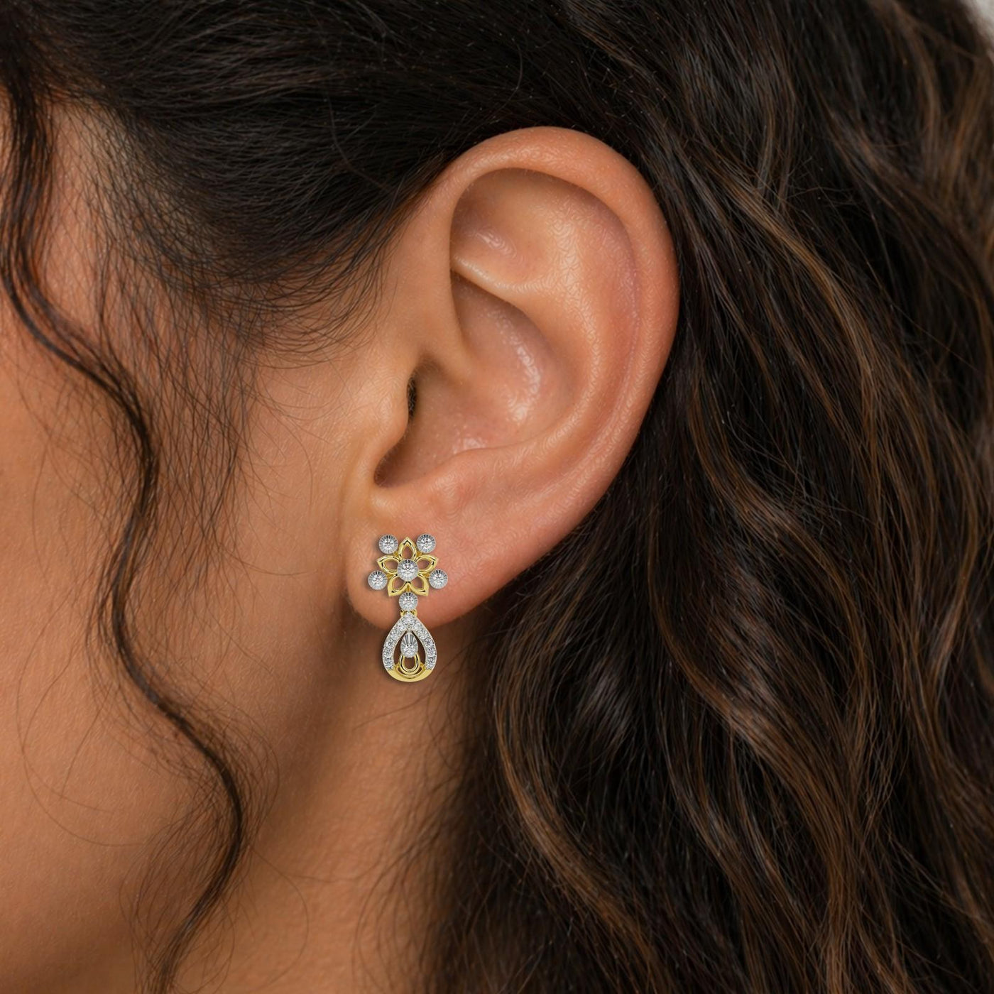 A pair of yellow gold earrings with diamond accents, featuring a floral design with teardrop shapes earring, close-up shot.
