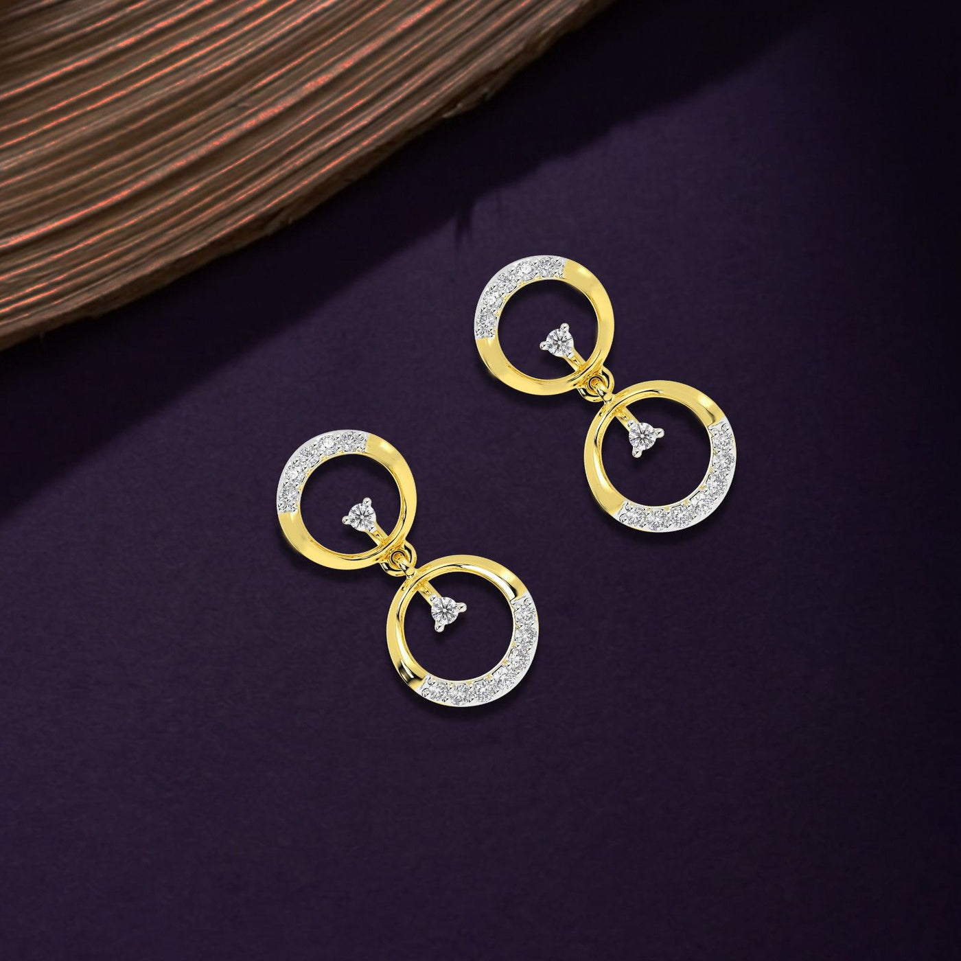 Gold and diamond earrings with circular designs on a purple background