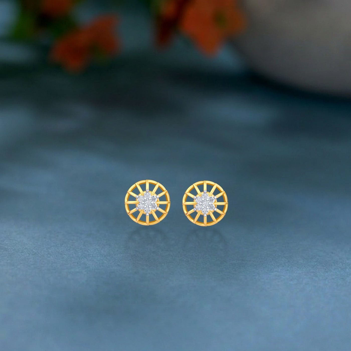 Gold and diamond stud earring with round-shaped on a teal surface.