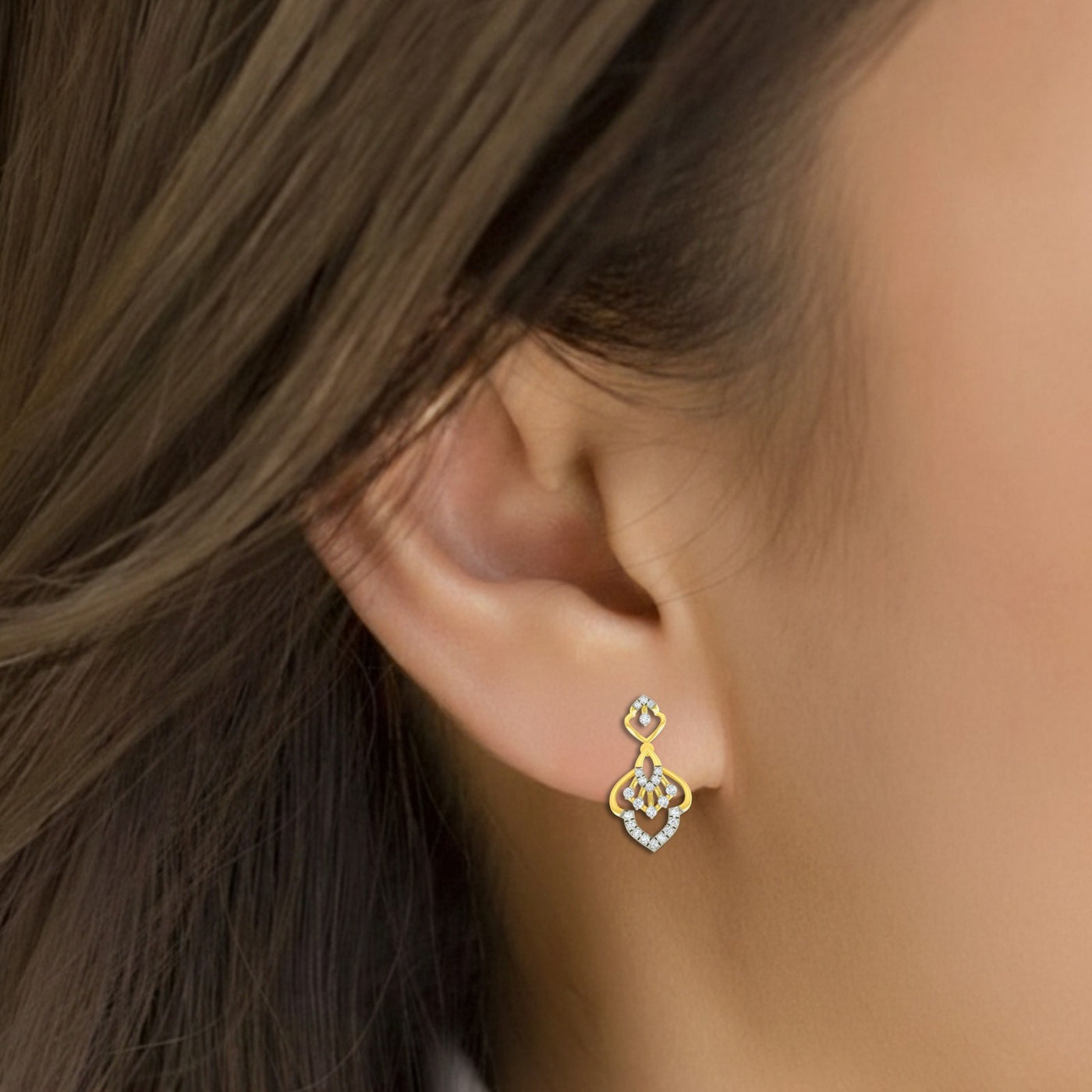 A close-up of a woman's ear wearing a gold and diamond earring with a decorative floral.
