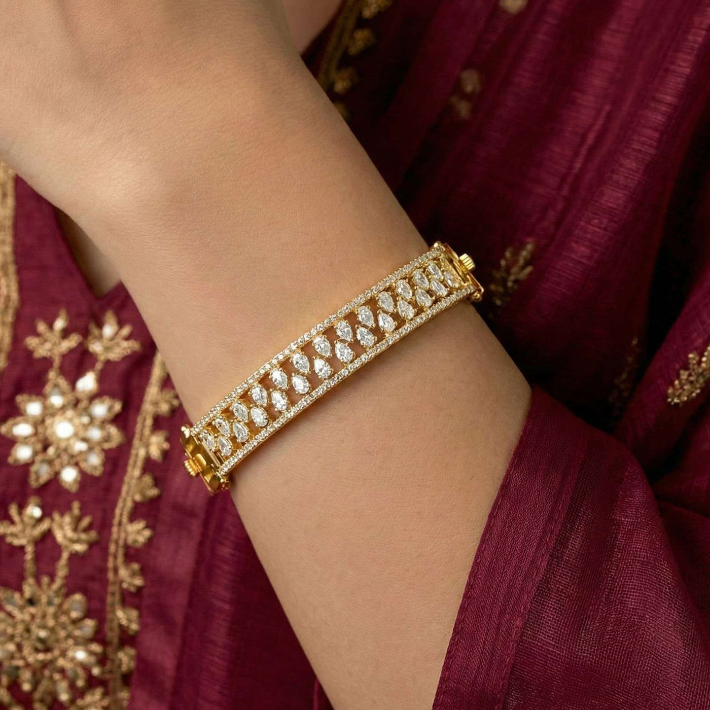 Gold bracelet with diamonds on a wrist against a maroon fabric background