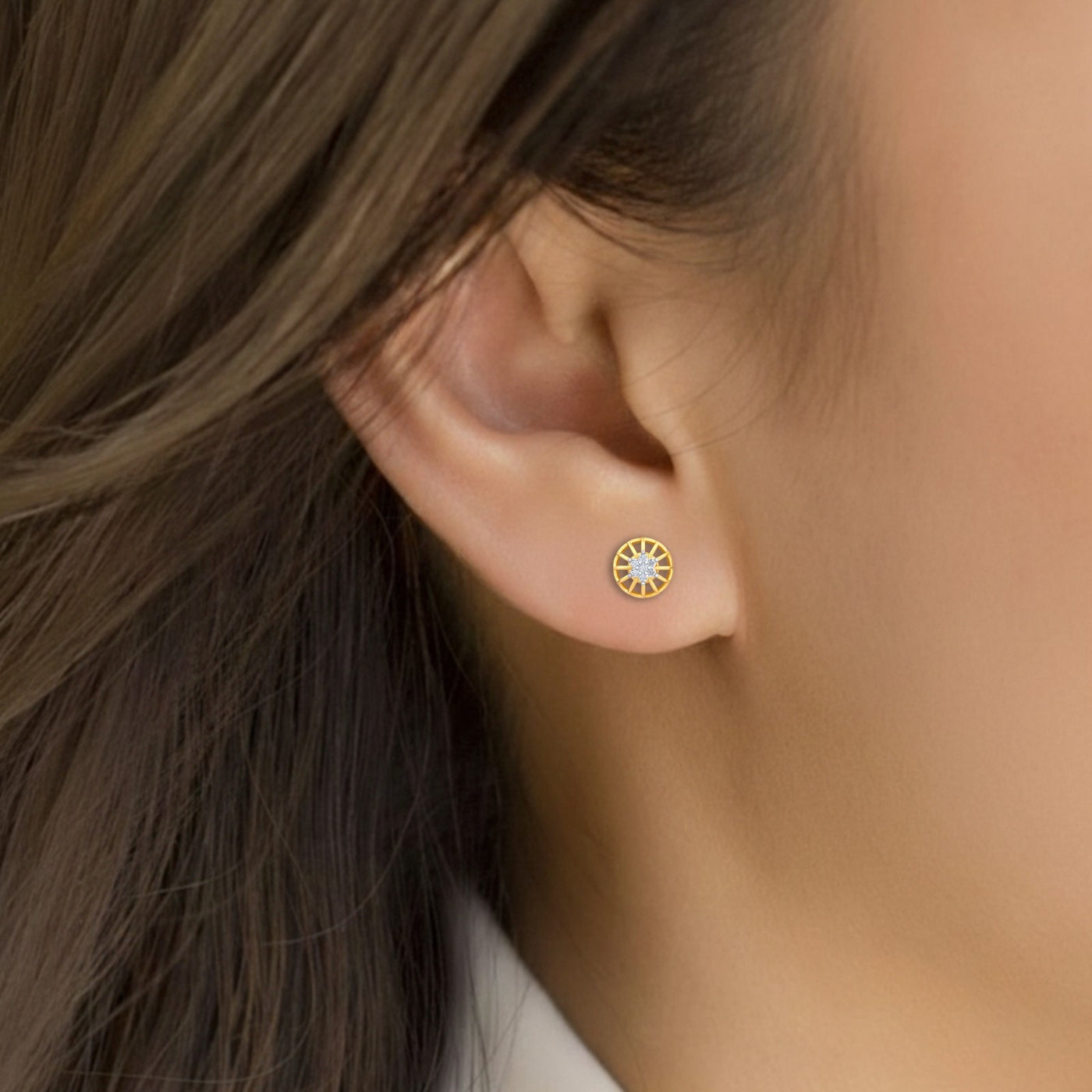 Close-up of an ear wearing a gold earring with a central diamond.