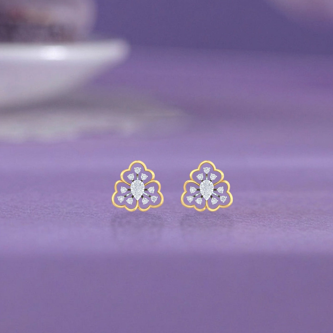 Gold and diamond stud earrings with floral-design on a purple fabric surface.