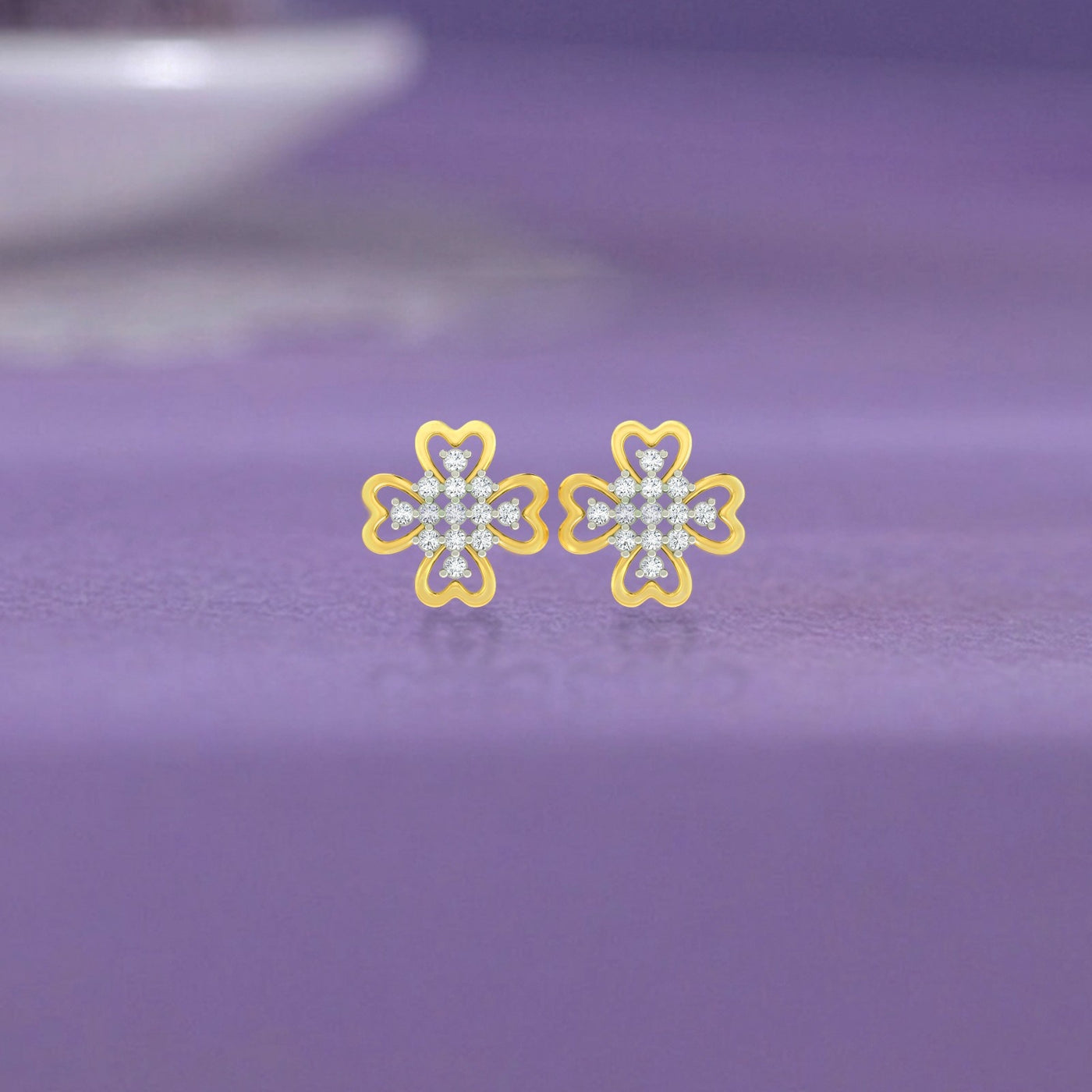 Gold and diamond floral-design earrings on a purple surface