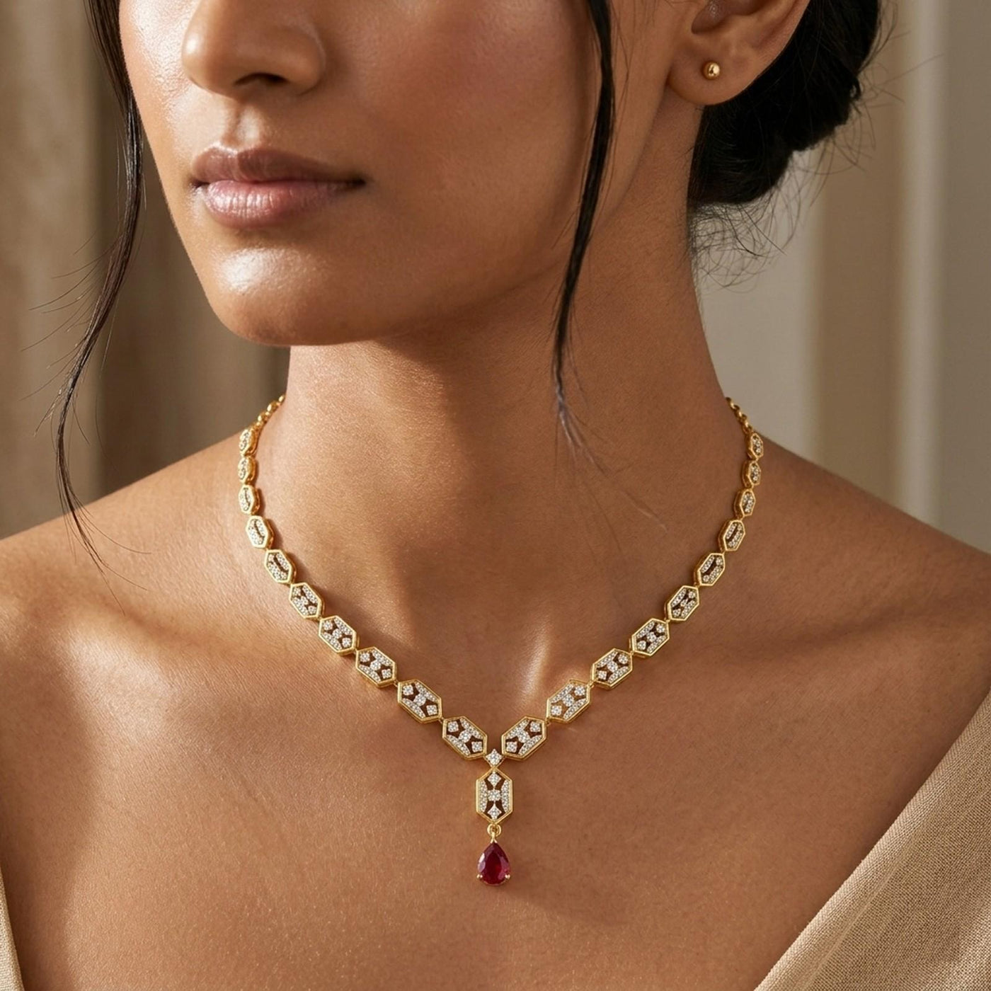 A close-up of a model wearing a delicate gold necklace with small red teardrop.