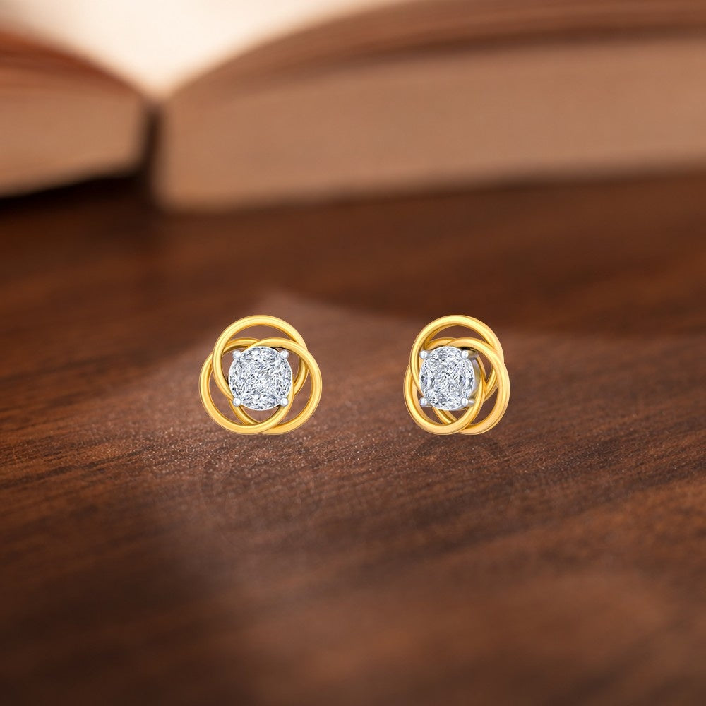 Gold and diamond floral-shaped stud earrings with center diamond on a wooden surface.