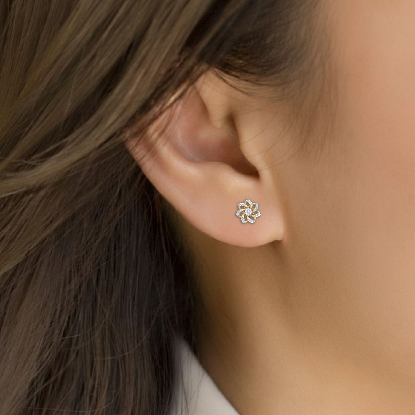 Close-up shot of a gold and diamond stud earring with floral-design.