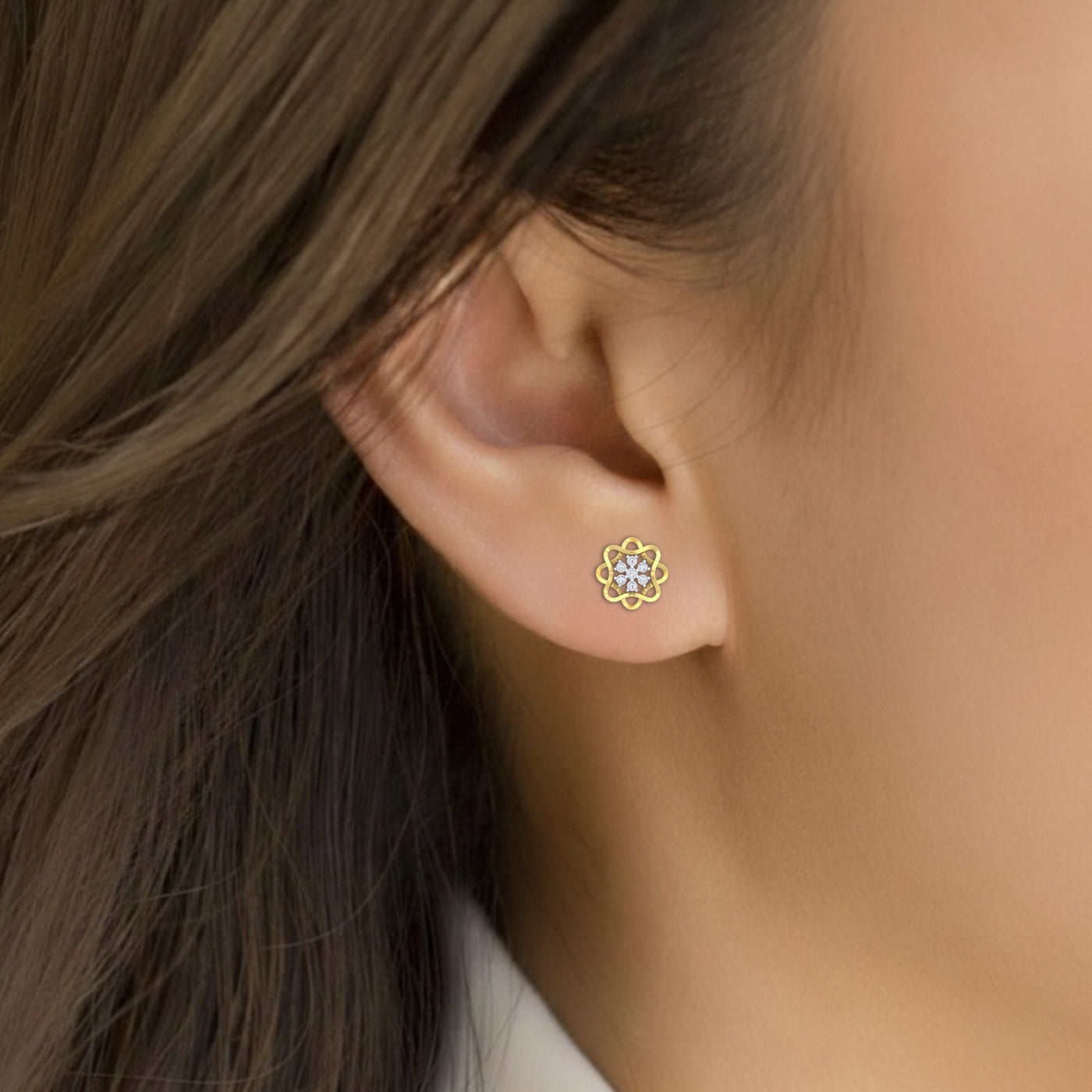 Close-up of an ear wearing a gold diamond stud earring with floral-design.