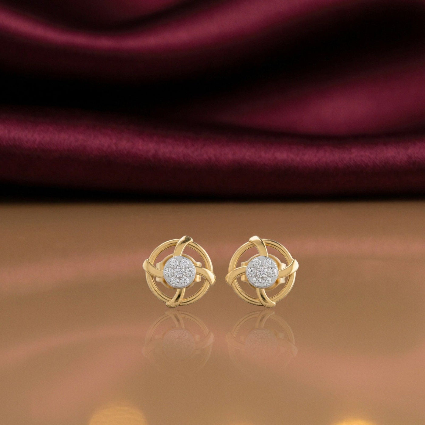 Gold and diamond earrings on a reflective surface.