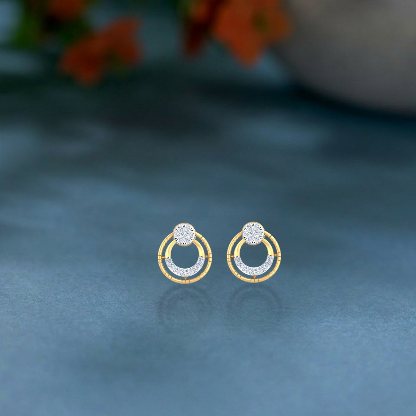 Gold and diamond stud earring with circular designs on a blue surface. 