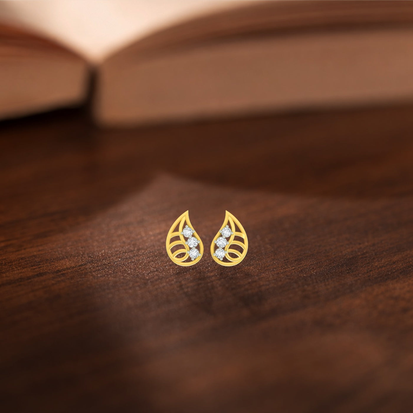 Gold and diamond teardrop-shaped earrings on a wooden surface