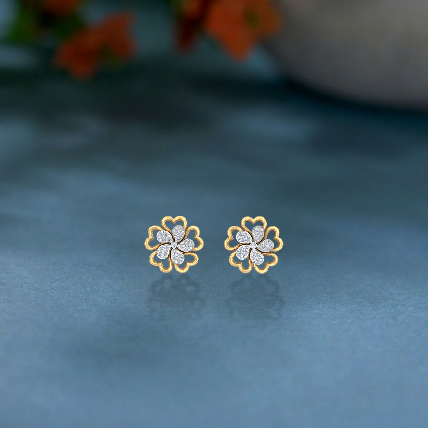 Gold and diamond stud earring with floral-shaped on a blue surface.