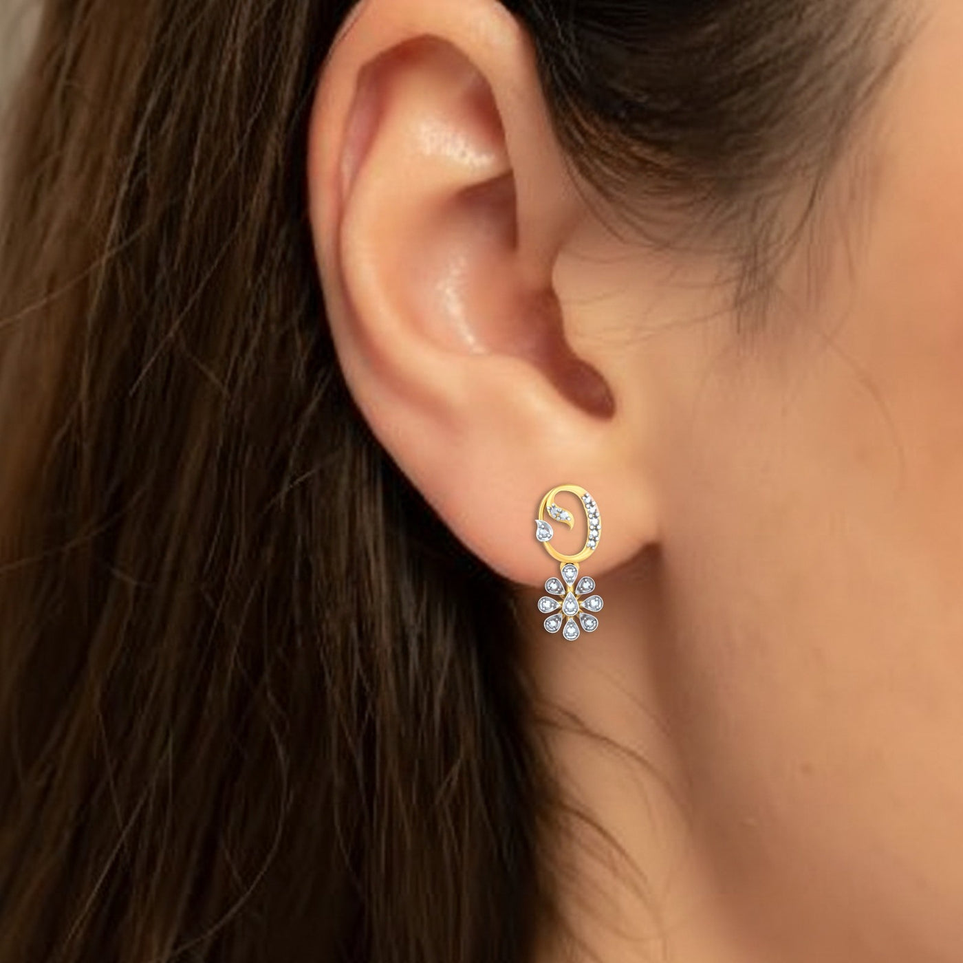 Close-up of an ear wearing a gold and diamond drop earring with floral design.