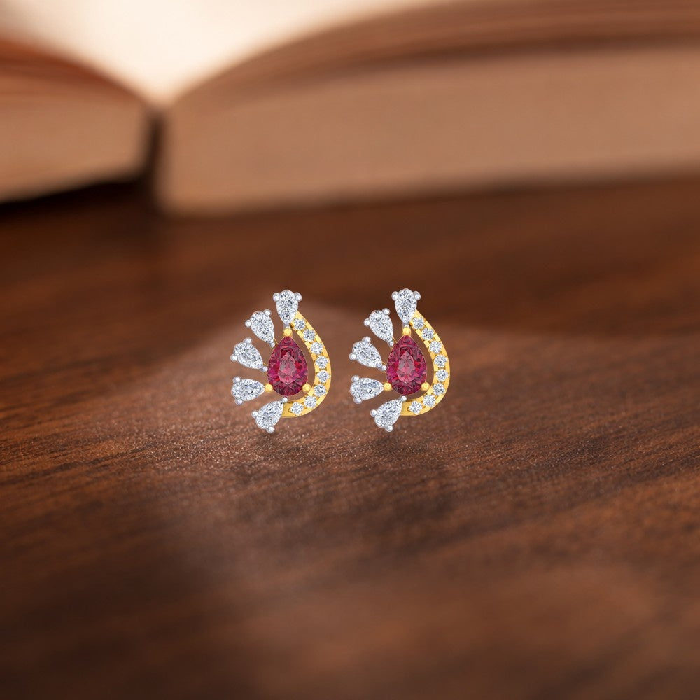 Pair of earrings with red gemstones and gold and diamond accents on a wooden surface.