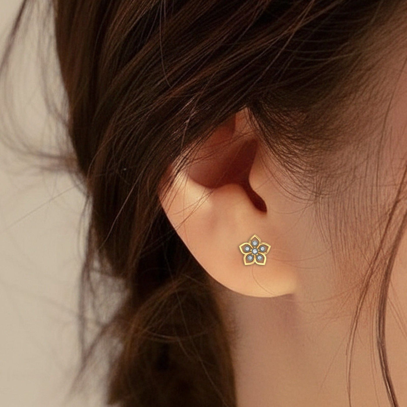 Close-up of an ear wearing a floral earring with a blurred background.